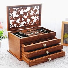 an open wooden jewelry box sitting on top of a table next to a vase with flowers