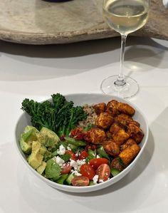 a white bowl filled with food next to a glass of wine