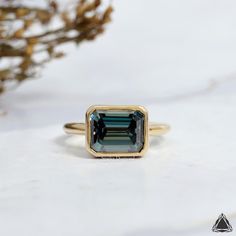 a green tourmaline ring sitting on top of a white table next to a plant