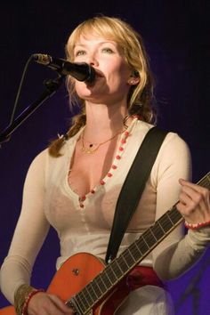 a woman singing into a microphone while playing an electric guitar