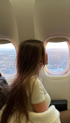 a woman sitting on an airplane seat looking out the window at the city below her