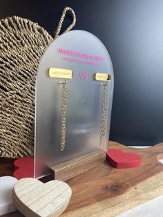 a pair of earrings on display in front of a heart shaped box with chain attached to it