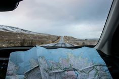 a map sitting on the dashboard of a car in front of a road with snow covered mountains