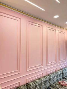 a room with pink walls and couches in front of the wall is decorated with gold trim