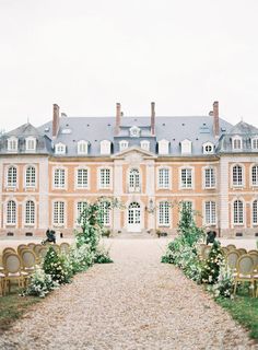 an outdoor ceremony with chairs and flowers in front of a large building that has many windows