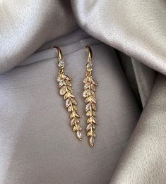 two pairs of gold tone earrings with clear stones and leaves hanging from the ends of them