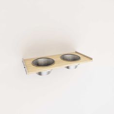 two metal bowls on a wooden shelf against a white wall, with one empty bowl in the middle