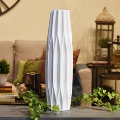 a tall white vase sitting on top of a wooden table next to a living room