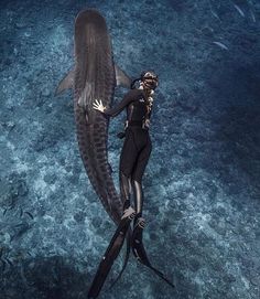 a woman in a black wetsuit standing next to a whale