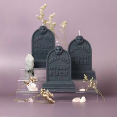 three cement tombstones sitting on top of a purple surface next to flowers and rocks