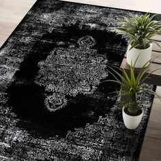 a black and white rug with an ornate design on the floor next to two potted plants