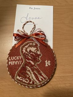 a red ornament with a brown ribbon on top of a wooden table next to a card