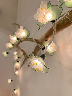 some lights are hanging from a branch with flowers on it and one light is turned on