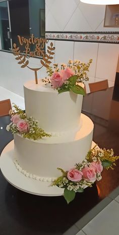 a three layer white cake with pink flowers and greenery on the top, sitting on a table in front of a mirror