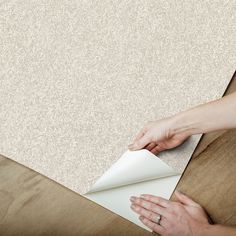 a person is holding a piece of paper on top of a wooden table with a white wallpaper