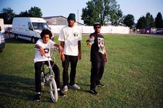 three young men standing next to each other on top of a grass covered field with a bicycle