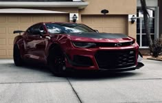 a red chevrolet camaro parked in front of a house