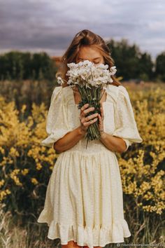 a woman in a white dress holding flowers and looking at the camera with her eyes closed