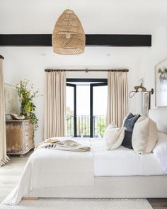 a white bed sitting in a bedroom next to a wooden dresser and window with curtains