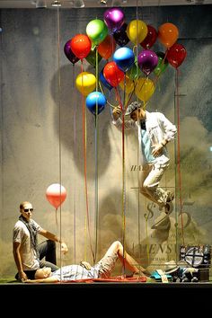 two men sitting on the ground in front of a display with balloons attached to it