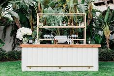 an outdoor bar set up in the middle of some grass with plants and flowers behind it