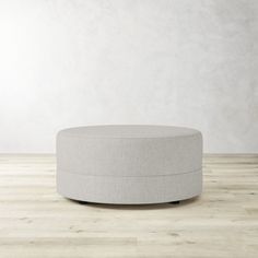 a round ottoman sitting on top of a hard wood floor next to a white wall