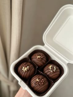 a hand holding a white container filled with chocolates