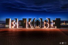 the word be kobe is lit up at night in front of a cityscape