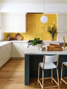 a kitchen with white cabinets and yellow backsplash, three chairs in front of the island