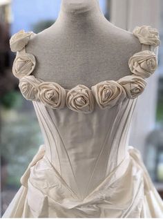 a white wedding dress with roses on the bustle and neckline is shown in front of a mannequin