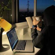 a person sitting at a desk with a laptop and book in front of their face