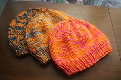 three knitted hats sitting on top of a wooden table