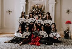 a group of women sitting on top of a floor holding up white and black fans