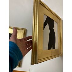 a person is holding up a painting in front of a gold frame with a woman's silhouette on it