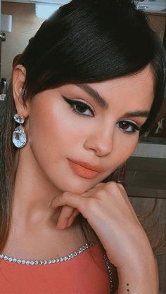 a woman with dark hair and earrings posing for the camera in a red dress, looking at the camera