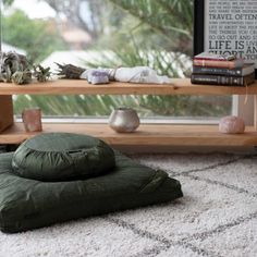 a green pillow sitting on top of a white rug next to a wooden shelf filled with books