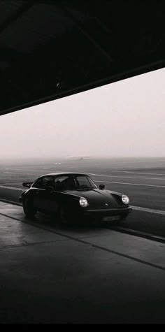 a black and white photo of a car driving down the road with fog in the background