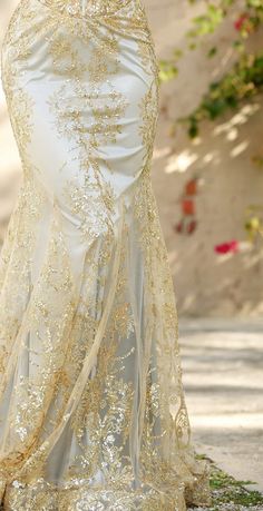 a woman in a white and gold dress standing on the street with her hands behind her back