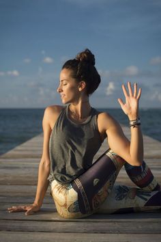 a woman sitting on top of a wooden dock next to the ocean holding her hands up