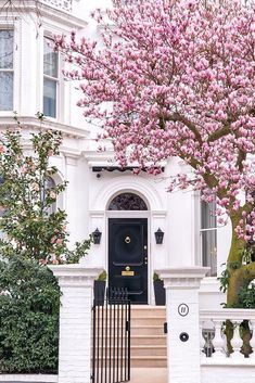 a tree with pink flowers is in front of a white house and steps leading up to the door