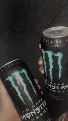 two cans of monster energy drink being held by someone