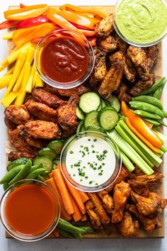 a platter with chicken wings, vegetables and dips