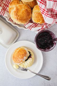 biscuits and jam are on plates next to a bowl of blueberry jam, with a red checkered napkin