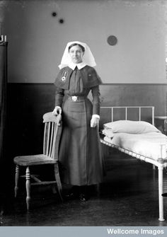 an old black and white photo of a woman in uniform standing next to a bed