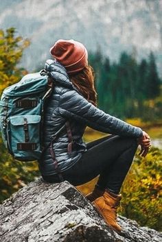 a woman sitting on top of a rock with a backpack in her lap looking at the mountains