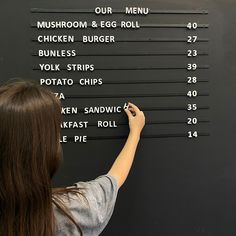 a woman writing on a blackboard with lots of words written on it and numbers in front of her