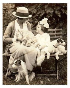 an old black and white photo of two women sitting on a bench with their dogs