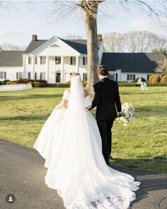 the bride and groom are walking down the road towards their wedding venue in front of the large white house