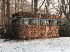 a building made out of logs sitting in the snow next to some trees and bushes