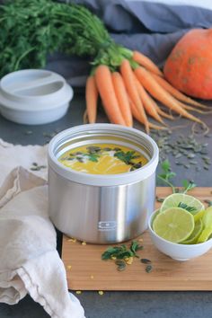 a bowl of soup with carrots and lime on a cutting board